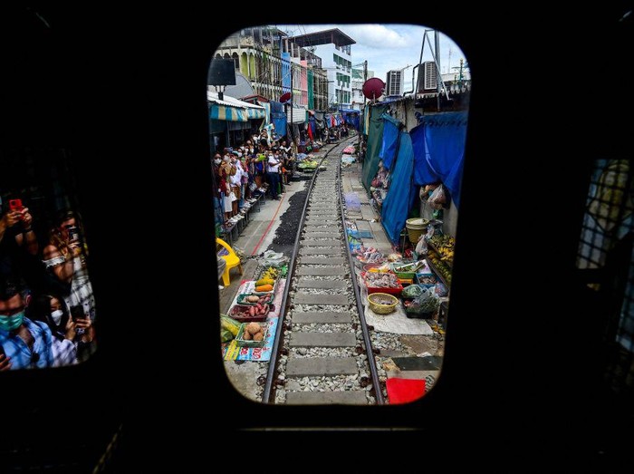 TOPSHOT - This photograph taken on June 4, 2022 shows a passenger train passing through the Mae Klong railway market in Samut Songkhram province, around 80 kms (50 miles) southwest of Bangkok. - Six times a day at the market, local customers and foreign tourists scramble into nooks and crannies while vendors calmly move their woven baskets of goods away from the tracks and close their umbrellas. - TO GO WITH Thailand-tourism-railway-market,FOCUS by Lisa MARTIN (Photo by Manan VATSYAYANA / AFP) / TO GO WITH Thailand-tourism-railway-market,FOCUS by Lisa MARTIN (Photo by MANAN VATSYAYANA/AFP via Getty Images)