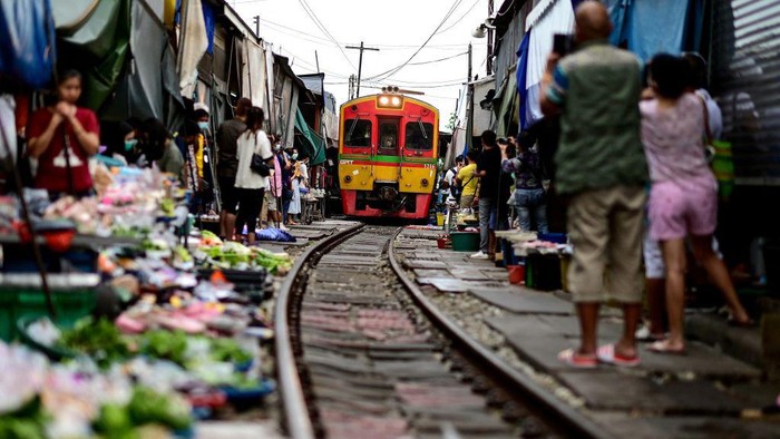 Sensasi Belanja di Pasar Mepet Rel Kereta di Thailand TOPSHOT - This photograph taken on June 4, 2022 shows a passenger train passing through the Mae Klong railway market in Samut Songkhram province, around 80 kms (50 miles) southwest of Bangkok. - Six times a day at the market, local customers and foreign tourists scramble into nooks and crannies while vendors calmly move their woven baskets of goods away from the tracks and close their umbrellas. - TO GO WITH Thailand-tourism-railway-market,FOCUS by Lisa MARTIN (Photo by Manan VATSYAYANA / AFP) / TO GO WITH Thailand-tourism-railway-market,FOCUS by Lisa MARTIN (Photo by MANAN VATSYAYANA/AFP via Getty Images)