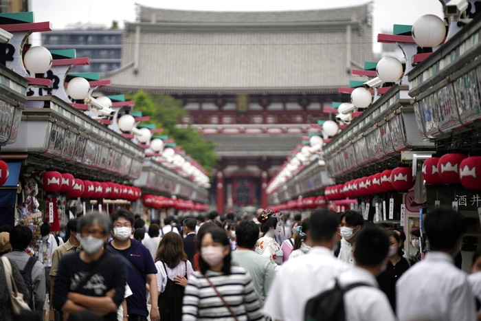 Foreign tourists wearing protective masks to help curb the spread of the coronavirus take a selfie at a shopping street at the Asakusa district Friday, June 10, 2022, in Tokyo. Japan on Friday eased its borders for foreign tourists and began accepting applications, but only for those on guided package tours who are willing to follow mask-wearing and other antivirus measures as the country cautiously tries to balance business and infection worries. (AP Photo/Eugene Hoshiko)