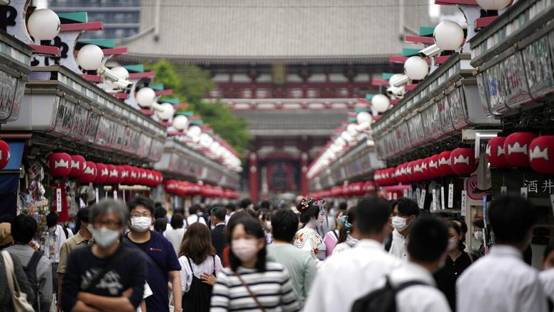 Foreign tourists wearing protective masks to help curb the spread of the coronavirus take a selfie at a shopping street at the Asakusa district Friday, June 10, 2022, in Tokyo. Japan on Friday eased its borders for foreign tourists and began accepting applications, but only for those on guided package tours who are willing to follow mask-wearing and other antivirus measures as the country cautiously tries to balance business and infection worries. (AP Photo/Eugene Hoshiko)