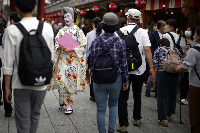 Foreign tourists wearing protective masks to help curb the spread of the coronavirus take a selfie at a shopping street at the Asakusa district Friday, June 10, 2022, in Tokyo. Japan on Friday eased its borders for foreign tourists and began accepting applications, but only for those on guided package tours who are willing to follow mask-wearing and other antivirus measures as the country cautiously tries to balance business and infection worries. (AP Photo/Eugene Hoshiko)