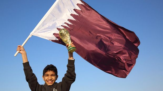 DOHA, QATAR - JANUARY 29: A football fan holding the maroon and white national flag of Qatar with a replica of the FIFA World Cup Trophy in Doha, Qatar, the host venue for the FIFA World Cup Final 2022 (Photo by Matthew Ashton - AMA/Getty Images)
