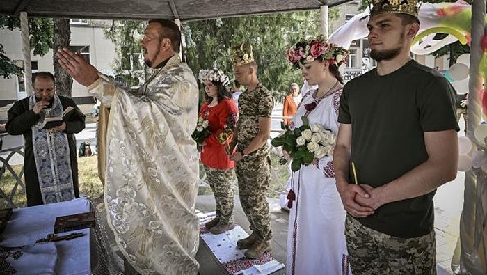 Bertemu di Medan Perang, 2 Pasang Prajurit Ini Menikah Ukrainian soldiers Kristina (2nd R) and Vitalii Orlich, both 23, and Khrystyna Lyuta (L), 23, with Volodymyr Mykhalchuk, 28, get married in the city of Druzhkivka, eastern region of Donbas on June 12, 2022. (Photo by ARIS MESSINIS / AFP) (Photo by ARIS MESSINIS/AFP via Getty Images)