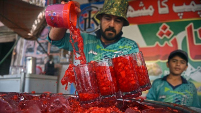 'Es Semangka', Minuman Penyegar Jiwa yang Satukan India-Pakistan In this photograph taken on May 25, 2022, a vendor prepares to serve Rooh Afza watermelon beverages to customers along a roadside stall in Karachi. - Pakistan and India have fought three wars and countless skirmishes, but as summers get hotter with climate change, their peoples are united by love for a cooling 115-year-old pink libation with a secret recipe. - TO GO WITH 'India-Pakistan-Lifestyle-History-Climate', FOCUS (Photo by Rizwan TABASSUM / AFP) / TO GO WITH 'India-Pakistan-Lifestyle-History-Climate', FOCUS (Photo by RIZWAN TABASSUM/AFP via Getty Images)