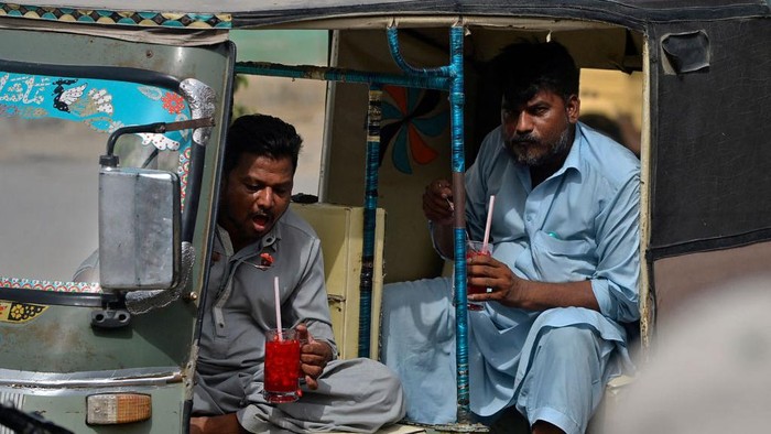 In this photograph taken on May 25, 2022, men drink Rooh Afza watermelon beverages while sitting in an auto rickshaw near a roadside stall in Karachi. - Pakistan and India have fought three wars and countless skirmishes, but as summers get hotter with climate change, their peoples are united by love for a cooling 115-year-old pink libation with a secret recipe. - TO GO WITH 'India-Pakistan-Lifestyle-History-Climate', FOCUS (Photo by Rizwan TABASSUM / AFP) / TO GO WITH 'India-Pakistan-Lifestyle-History-Climate', FOCUS (Photo by RIZWAN TABASSUM/AFP via Getty Images)