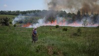 Seorang penduduk setempat melihat rumput yang terbakar setelah penembakan, di tengah serangan Rusia di Ukraina, dekat kota Bakhmut, wilayah Donetsk.