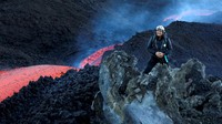Dalam foto yang dipotret pada Sabtu (11/6/2022), seorang pendaki berfoto dengan latar aliran panjang lava merah panas mengalir di kawah tenggara Gunung Etna, Italia.