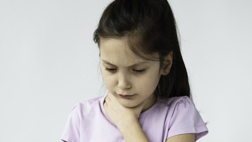 Little girl is holding her throat in pain in front of white background.