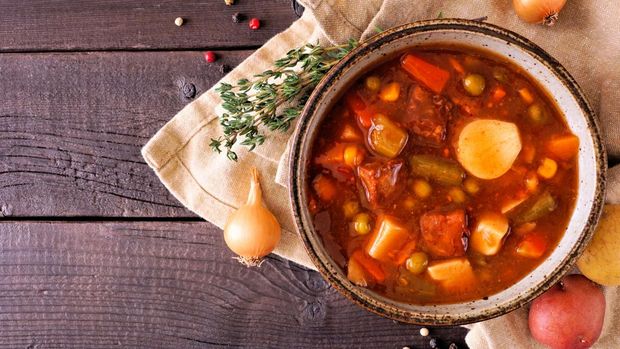 Homemade beef vegetable soup. Top down view table scene on a dark wood background with copy space.