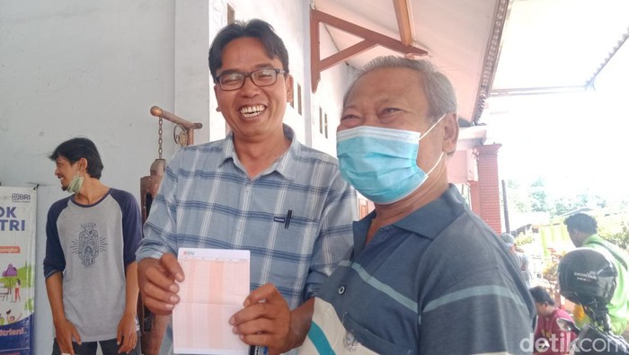 Kakek Subagyo (bermasker) tertawa usai menerima ganti rugi Rp 4 juta dari proyek Tol Jogja-Solo. Subagya berfoto bersama Kades Demak Ijo, Kecamatan Karangnongko, Ery Karyanto yang menunjukkan buku rekening Bagyo.