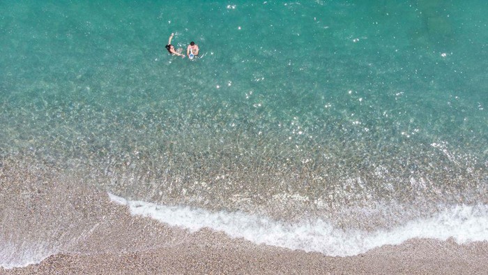 Aerial images from a drone of the coast of Rethymno town with the long beach and the beach bars in Creta island. People are seen enjoying the sun under the umbrella at the beach bar or swimming in the crystal clear sea. Rethymno is a historic Mediterranean beach town on the northern coast of Crete, laying on the Aegean Sea with a population of 40.000 people. A touristic destination with a historic Venetian port and town, Archaeological sites, endless sandy beaches, watersports, nice beautiful traditional taverns, and a big variety of hotels. Tourism is bouncing back with reservations exceeding the pre-pandemic numbers, putting Greece and the Greek islands on high demand. Tourists travel after the Covid-19 Coronavirus pandemic. Rethimno, Crete island, Greece on June 13, 2022 (Photo by Nicolas Economou/NurPhoto via Getty Images)