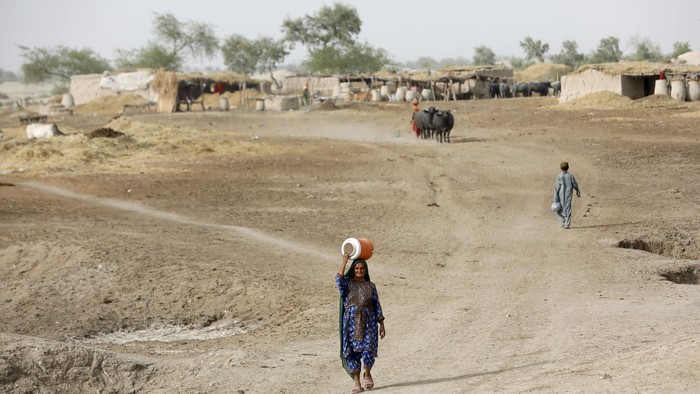 A woman walks to fetch water from a nearby hand-pump with a water cooler on her head, during a heatwave, on the outskirts of Jacobabad, Pakistan, May 16, 2022. Last month Jacobabad became the hottest city on Earth. Women are especially vulnerable to rising temperatures in poor countries on the frontlines of climate change because many have little choice but to work through their pregnancies and soon after giving birth, according to interviews with more than a dozen female residents in the Jacobabad area as well as half a dozen development and human rights experts.  REUTERS/Akhtar Soomro  SEARCH 