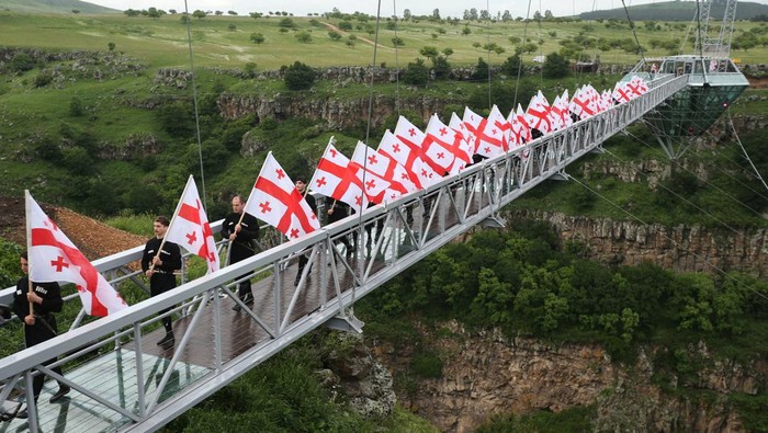 GEORGIA-TOURISM/BRIDGE People carry Georgian flags as they walk on the glass bridge over Dashbashi Canyon during the opening ceremony outside the town of Tsalka, Georgia June 14, 2022. REUTERS/Irakli Gedenidze