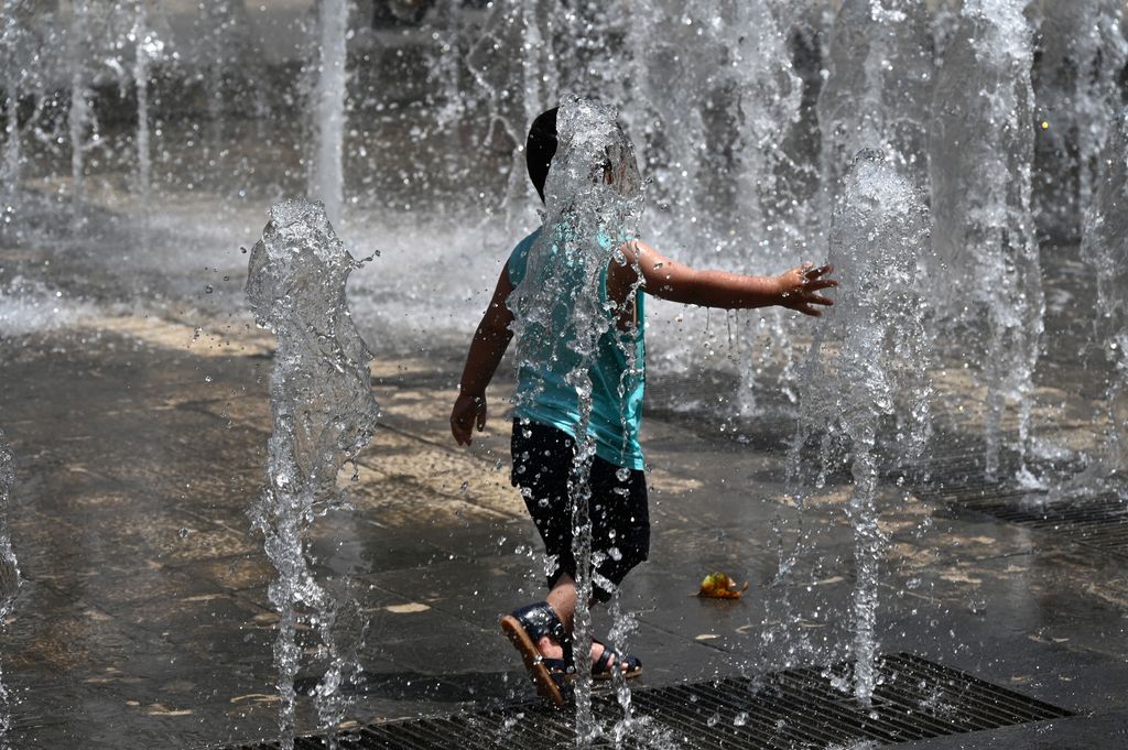Seorang anak mendinginkan badan saat gelombang panas melanda di air mancur di pusat kota Montpellier, Prancis selatan, Selasa (14/6/2022). (Photo by PASCAL GUYOT/AFP via Getty Images)