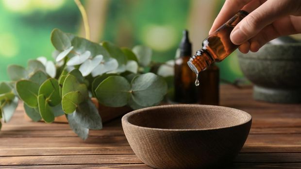 Woman pouring eucalyptus essential oil into bowl on wooden table
