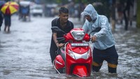 Dua orang pria mendorong skuternya melewati jalan yang banjir. Guwahati telah mengalami curah hujan hingga 81,5 mm dalam 24 jam terakhir yang termasuk kategori hujan lebat.