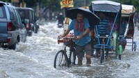 Seorang pria membawa tabung gas di sepedanya dan menyeberangi jalan yang banjir saat hujan deras di Guwahati, Assam, India, Kamis, 16 Juni 2022. Assam berada di sisi timur India, berbatasan langsung dengan Myanmarm Bangladesh dan Bhutan.