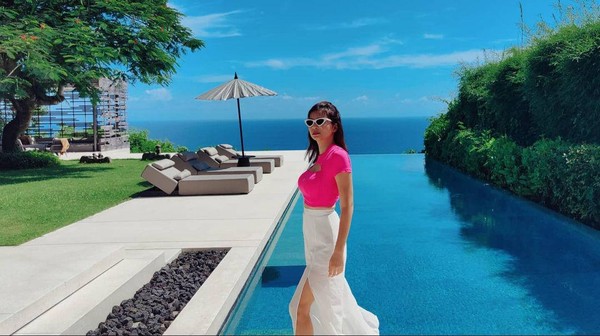 Mengenakan atasan pink dan bawahan putih, ibu anak satu ini terlihat manis dan kontras sekali dengan birunya kolam renang dan langit Bali. (Instagram/@sandraolga)