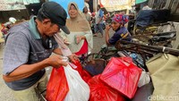 Seorang tukang becak menyusun belanjaan seorang warga yang hendak menaiki becak.