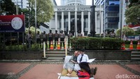 Dua peserta aksi yang menggambarkan pasangan suami istri itu tidur di atas kasur dengan memegang dokumen.