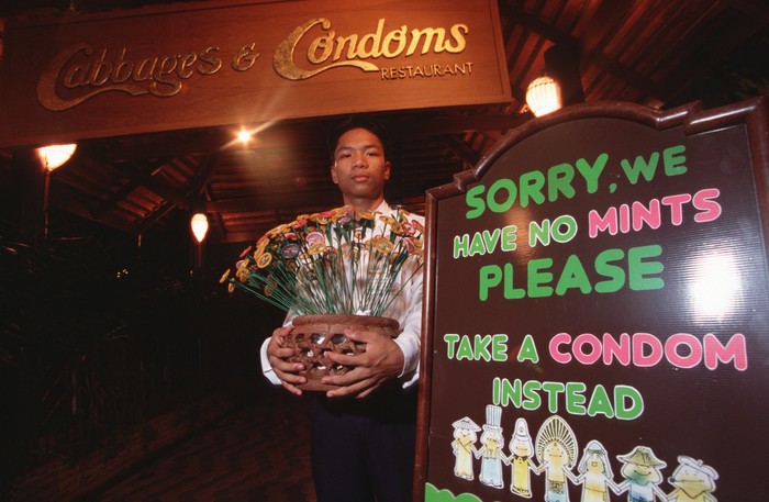 158608233 BANGKOK, THAILAND - 1994/02/01: A portrait of Mechai Viravaidya who is Thailand's leading anti AIDS activist sitting in the restaurant he founded called 'Cabbages and Condoms. Here he takes an 'after-dinner condom' instead of a mint! He has popularised condom use in Thailand and has created popular family planning clinics in the country. Such is his fame that condoms in Thailand are now known as 'Mechais'.. (Photo by Peter Charlesworth/LightRocket via Getty Images)