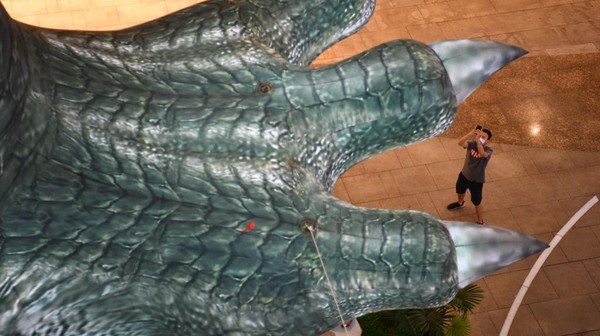 Bukan dinosaurus sungguhan ya, melainkan hanya instalasi seni untuk menarik pengunjung. Oh iya, kaki dino tersebut tidak menyentuh lantai mal melainkan tergantung di langit-langit.