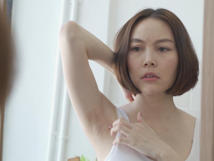 reflection mirror Asian female worry about black armpit with hair growing in bathroom at home. dark underarms concept. short hair woman looking mirror concern worried and Lack of confidence. problem.