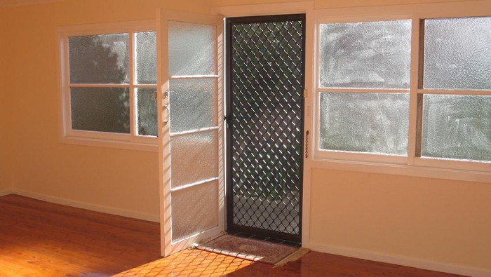 Sun shining through the doorway of an empty room with hardwood floorboards.