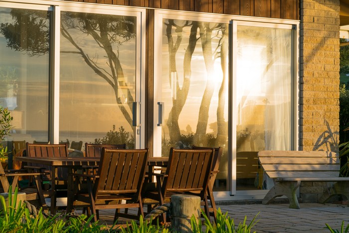 Waterfront home exterior with outdoor furniture and large windows reflecting sunrise over the sea