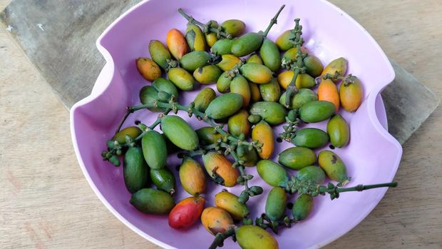 Gnetum gnemon fruit in a purple bowl on a wooden chopping board