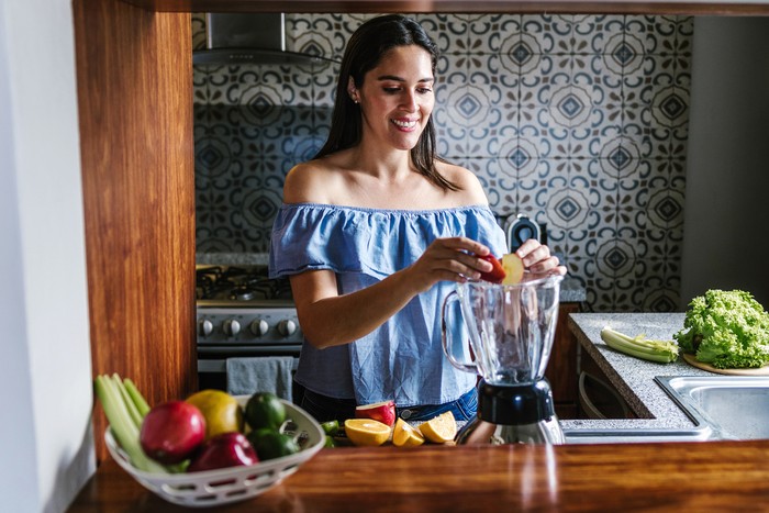 Ilustrasi Blender Fitur Lengkap Latin Woman making green smoothie or Detox juice in kitchen at Home in healthy eating concept in Mexico
