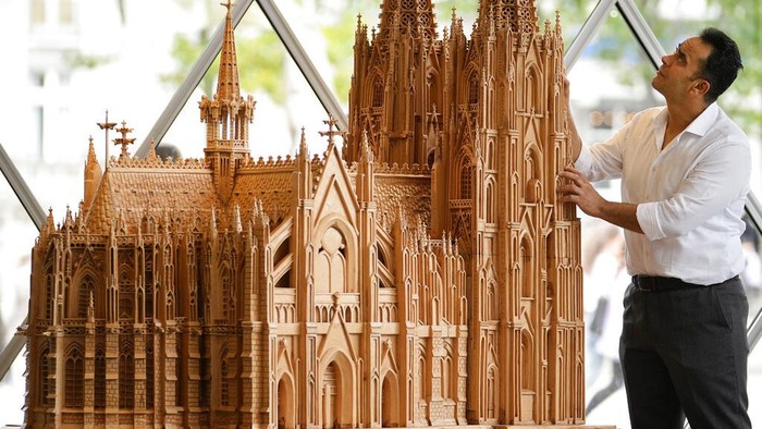 Fadel Alkhudr from Syria poses beside his wooden model of the word heritage Cologne Cathedral on display at the Domforum in Cologne, Germany, Monday, June 20, 2022. Fadel Alkhudr, 42, a woodcarver and artist orginally from Aleppo, Syria, fled the war in his home country and arrived in the western german city of Cologne in 2015. In 2019 he started to carve the local Cologne Cathedral in his small basement - without any plans or drawings, using only cell phone photos of the cathedral as a template. (AP Photo/Martin Meissner)