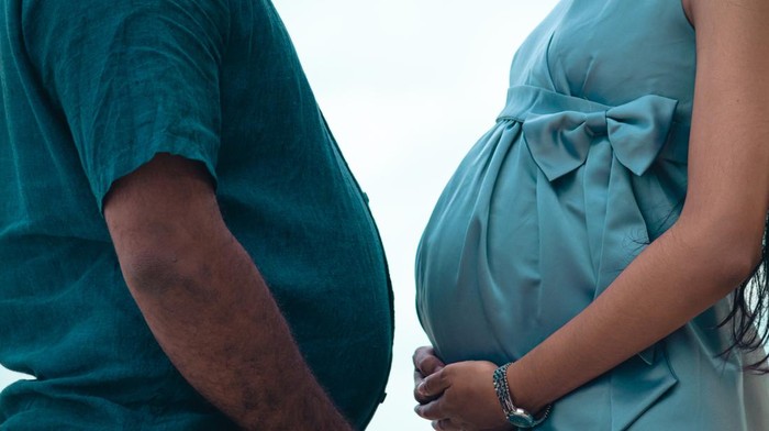cuti melahirkan Pregnant belly and a beer belly against each other together close up, holding bellies by both hands side view, couple goals concept.