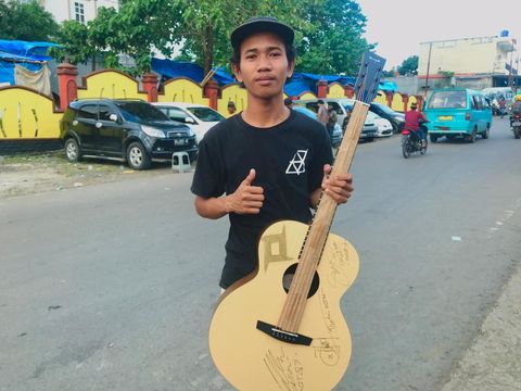 Pengamen Asrianto memarkan gitar pemberian Tantri Kotak.