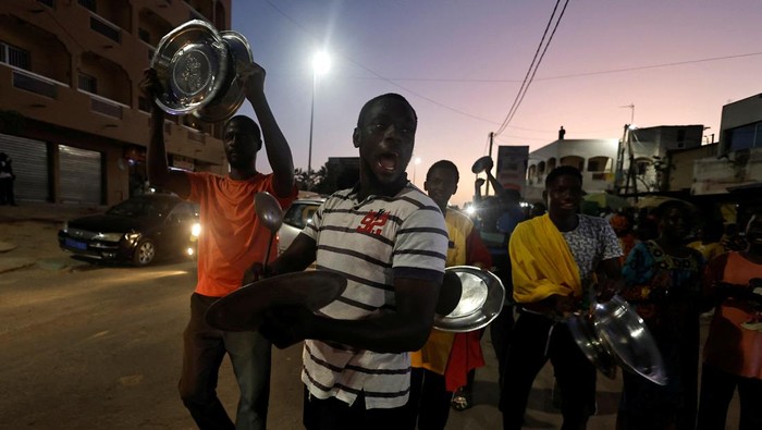 Potret Warga Senegal Pukul Panci dan Wajan di Jalan Ibrahima Soumare, 47, a supporter of Senegal's main opposition coalition Yewwi Askan Wi holds signs glued on pot lids during a protest over the disqualification of their national list for the July 31 legislative election in Dakar, Senegal, June 22, 2022. REUTERS/Zohra Bensemra
