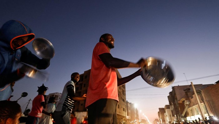 Potret Warga Senegal Pukul Panci dan Wajan di Jalan Ibrahima Soumare, 47, a supporter of Senegal's main opposition coalition Yewwi Askan Wi holds signs glued on pot lids during a protest over the disqualification of their national list for the July 31 legislative election in Dakar, Senegal, June 22, 2022. REUTERS/Zohra Bensemra