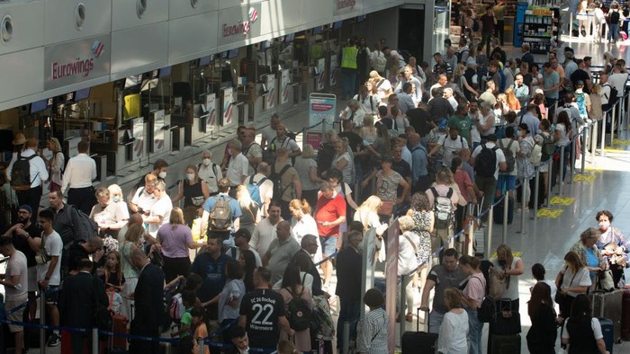 1241491262 polices are seen patrolling among the Travellers who are seen waiting in a long line at a security check point at Duesseldorf airport in Duesseldorf, Germany on June 22, 2022 as staff shortages continues causes the airport chaos during the holiday season (Photo by Ying Tang/NurPhoto via Getty Images)