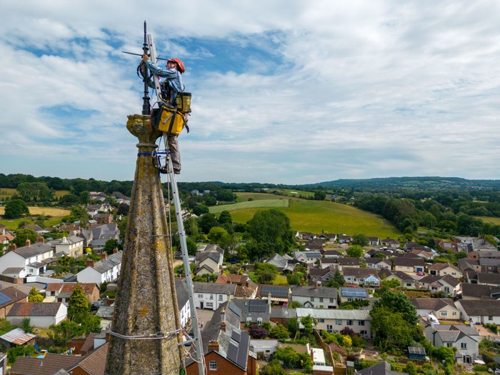 1404647766 UFFCULME, ENGLAND - JUNE 23: Arthur Needham from Vitruvius Building Conservation paints the lightning conductor on the steeple as part of restoration work at the top of St Maryβs Church, on June 23, 2022 in Uffculme, United Kingdom. (Photo by Finnbarr Webster/Getty Images)