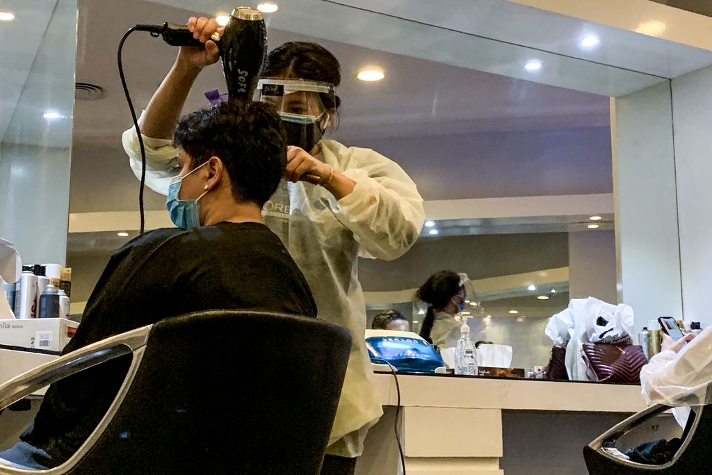 A hairdresser clad in face shield and mask blow-dries a client's hair at a women's beauty centre in Saudi Arabia's capital Riyadh on June 21, 2020, as the country begins to re-open following the lifting of a lockdown due to the COVID-19 coronavirus pandemic. (Photo by RANIA SANJAR / AFP) (Photo by RANIA SANJAR/AFP via Getty Images)