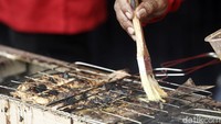 Seorang kader PDIP melumuri ikan dengan bumbu sambil terus mengipasi ikan yang dibakar.