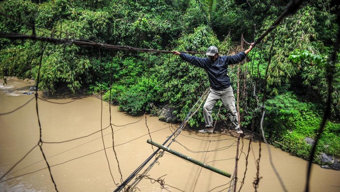 Warga menyeberangi sungai menggunakan jembatan kawat besi di Desa Salamnunggal, Kecamatan Cibeber, Kabupaten Cianjur, Jawa Barat, Sabtu (25/6/2022). Untuk menghemat jarak tempuh antar desa, warga terpaksa masih menggunakan jembatan tersebut serta berharap agar pemerintah terkait mampu membangun jembatan yang layak bagi warga sekitar. ANTARA FOTO/Raisan Al Farisi/rwa.