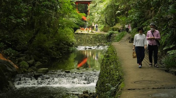 Dua orang warga berjalan di jalan sepatak di sepanjang sungai yang mengalir di taman Lembah Todoroki, Tokyo, Jepang.