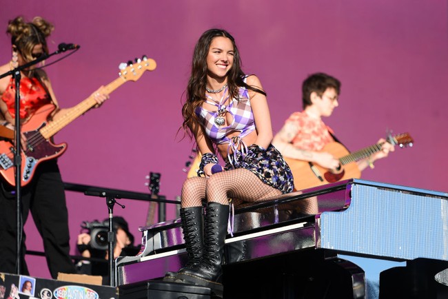 Melengkapi gaya seksi tersebut, sepasang boots tinggi bertali hitam yang menjadi andalan Olivia Rodrigo menyumbangkan kesan gahar. Sementara itu, rambut coklatnya yang panjang dibiarkan bebas tergerai. (Foto: Redferns/Matthew Baker)