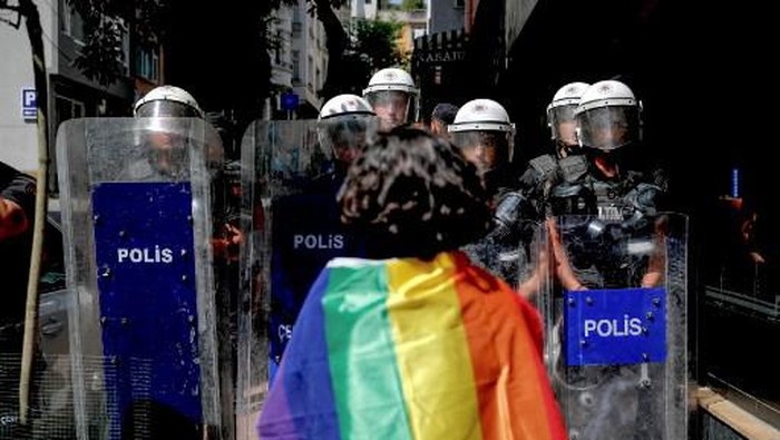 A participant faces riot policemen wearing a rainbow flag during a Pride march in Istanbul, on June 26, 2022. - Turkish police forcibly intervened in a Pride march in Istanbul, detaining dozens of demonstrators and an AFP photographer, AFP journalists on the ground said. The governors office had banned the march around Taksim Square in the heart of Istanbul but protesters gathered nearby under heavy police presence earlier than scheduled. (Photo by KEMAL ASLAN / AFP)