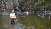 Putin memegang alat pancing dan ikan yang ditangkapnya saat memancing di wilayah Siberia Tyva. AP/Alexei Nikolsky