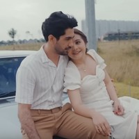 Gaya casual bisa diterapkan pada foto pre-wedding dengan konsep outdoor. Prilly tampil manis mengenakan gaun putih berpotongan leher square, sementara Reza Rahadian stylish dengan padanan kemeja stripe dan celana beige. Foto: Tangkapan Layar YouTube Prilly Latuconsina