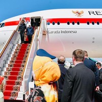 Tiba di Moskow, Iriana memadukan parka tersebut dengan hijab putih, celana panjang hitam dan sneakers senada. Gayanya selaras dengan Presiden Jokowi yang mengandalkan jaket bomber biru gelap beraksen putih pada bagian lengan, dan celana panjang serta sneakers serba hitam. (Foto: Anadolu Agency via Getty Images)