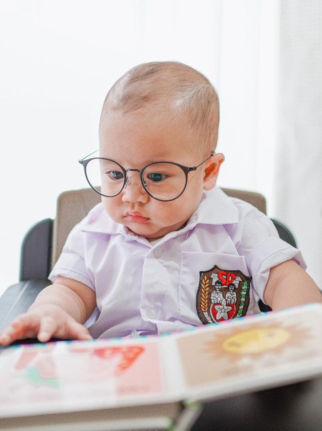 Sambil memakai kaca mata, Rayyanza tampak begitu serius melihat buku yang sedang dipegangnya. Gimana nih, sudah cocok jadi murid SD belum nih? Foto: Instagram/@raffinagita1717