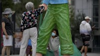 Anak-anak juga mengenakan masker, seperti anak yang berdiri di antara patung seni ini. Warga membawa anak-anak mereka bermain di kompleks gedung perkantoran komersial di Beijing. (AP News)