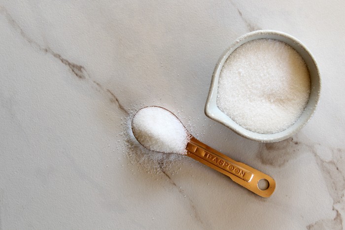 Sugar on a copper teaspoon and a cup of sugar. White marble copy space.